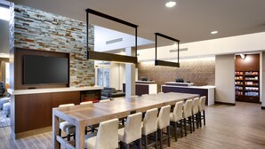 A modern kitchen with a long wooden table, built-in appliances, and a brick accent wall. - Residence Inn by Marriott Des Moines Ankeny (Ankeny)