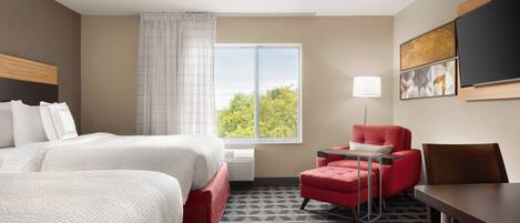 A hotel room with two beds, a red armchair, a table, and a large window with a view of trees.