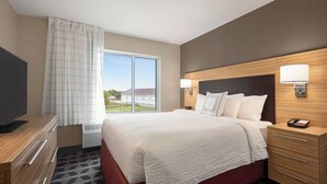 A hotel room with a large bed, a TV, a desk, and a window with curtains. - TownePlace Suites by Marriott Janesville (Janesville)