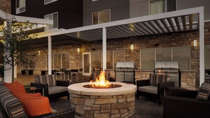 An outdoor patio with a stone fire pit, outdoor seating, and a grill area. - TownePlace Suites by Marriott Janesville (Janesville)