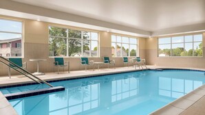 A swimming pool with chairs and tables, large windows, and a view of trees and buildings. - TownePlace Suites by Marriott Janesville (Janesville)