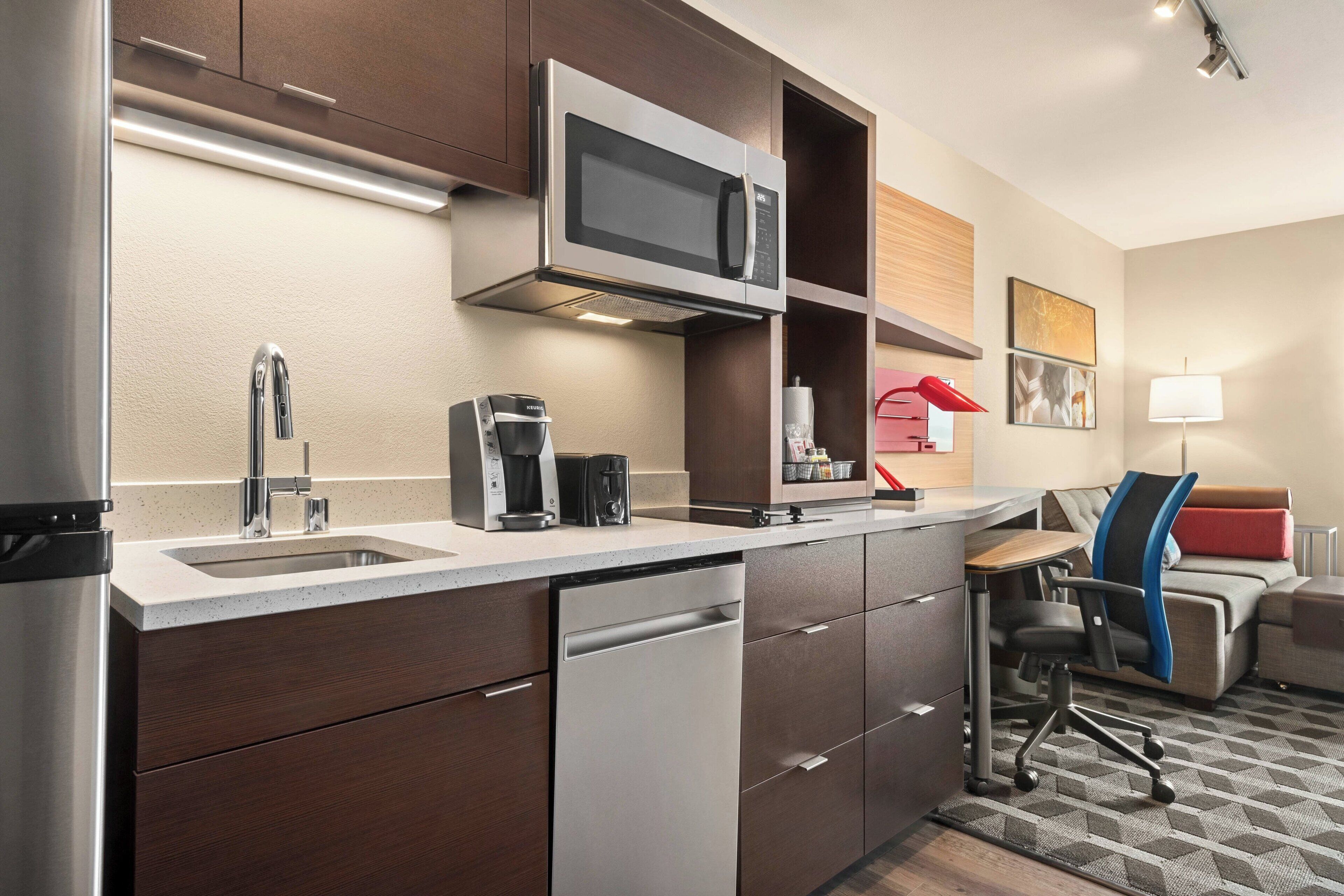A compact kitchen with a microwave, coffee maker, and dishwasher. There is a small seating area with a couch and a desk.