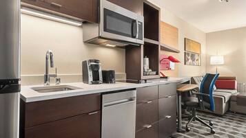 A compact kitchen with a microwave, coffee maker, and dishwasher. There is a small seating area with a couch and a desk.
