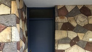 Ein Eingang mit einer Steinsäule, einer blauen Tür und einer kleinen blauen Platte auf der rechten Seite.
