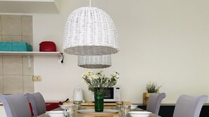Ein Esstisch mit Platzsets, einer Blumenvase und einer weißen gewebten Pendelleuchte.