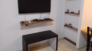 A living room with a mounted TV, wooden shelves, a black bench, and a tiled floor.