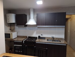 A compact kitchen with dark cabinets, a microwave, a stove, and a sink. - Departamento Tunuyan (Tunuyan)