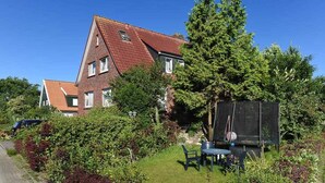 A two-story house with a red-tiled roof, surrounded by lush greenery and a trampoline in the backyard. - Vacation apartment Seestern - Holiday apartments Der Seehund, Haus Kajedeich in (Esens)