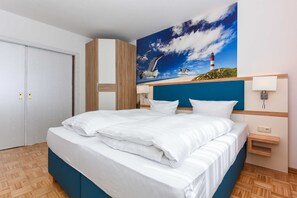 A hotel room with a large bed, a painting of a lighthouse and seagulls, a wooden wardrobe, and a nightstand with a lamp. - Vacation apartment Seestern - Holiday apartments Der Seehund, Haus Kajedeich in (Esens)