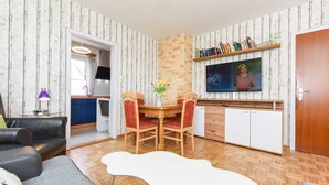 A living room with a sofa, a coffee table, a dining table with chairs, a TV, and a kitchen area with a sink and cabinets. - Vacation apartment Seestern - Holiday apartments Der Seehund, Haus Kajedeich in (Esens)