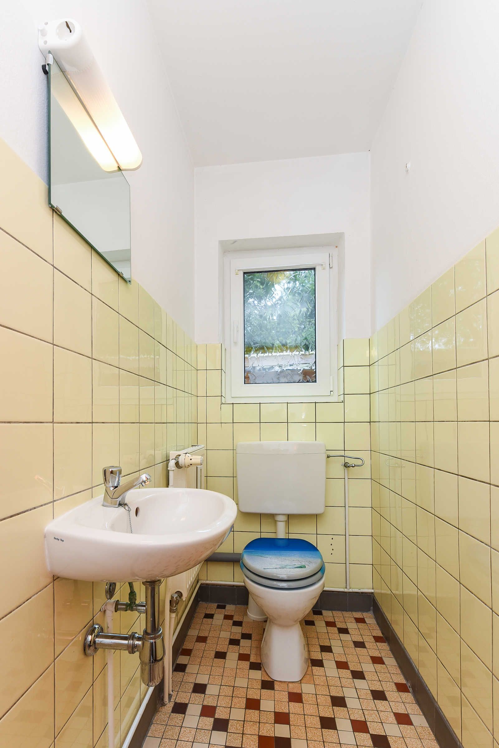 Une petite salle de bain avec des toilettes, un lavabo et une fenêtre située au-dessus des toilettes.
