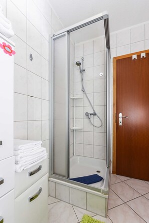 A walk-in shower with a glass door, a wooden door to the right, and a tiled floor. - Vacation apartment Seestern - Holiday apartments Der Seehund, Haus Kajedeich in (Esens)