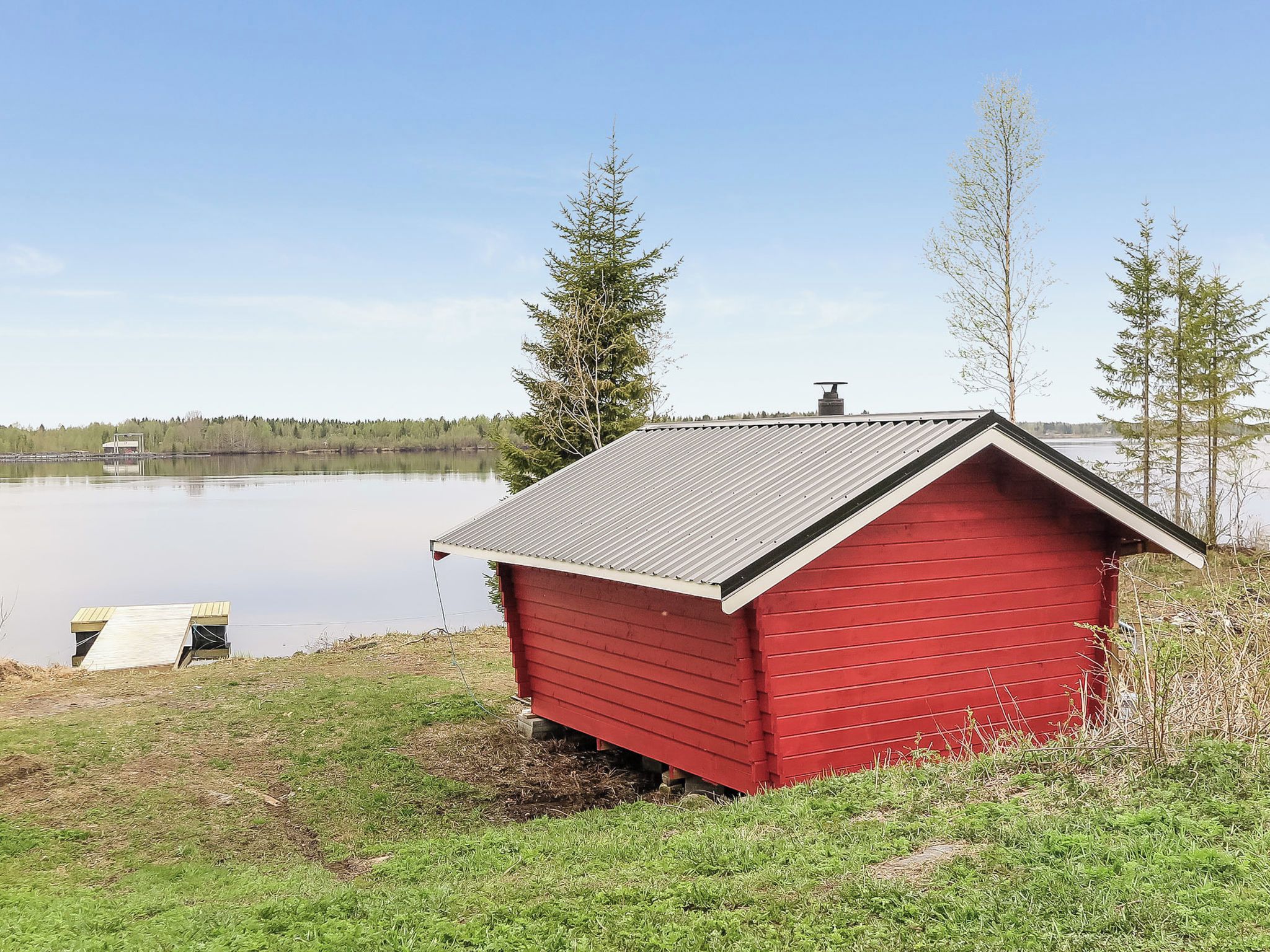 En röd trästuga vid en stilla sjö under en klar himmel.