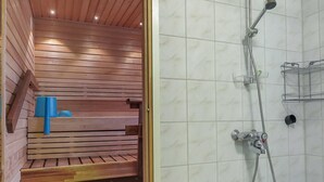 A sauna with wooden benches and a shower area with a tiled wall and a metal rack. - Itäkoski 1 by Interhome (Keminmaa)