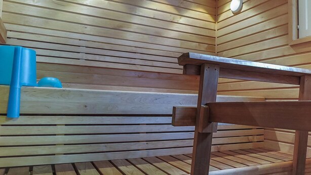 A wooden bench with a metal frame in a room with wooden panel walls and a ceiling light. - Itäkoski 1 by Interhome (Keminmaa)