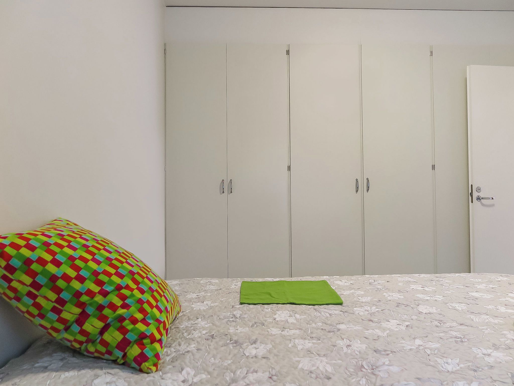A bedroom with a bed, a colorful pillow, and a wardrobe.