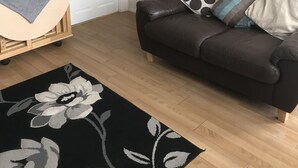 Ett vardagsrum med en brun lädersoffa, en svartvit matta med blommönster, en träkärra och vita dörrar.