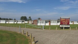 En campingplats med en skylt som anger hastighetsbegränsningen, en skylt för värdshuset Dutchy's och ett inhägnat område med husvagnar.