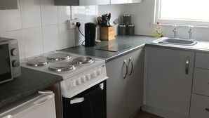 Ett kompakt kök med vita skåp, en spis, ett handfat och ett fönster.