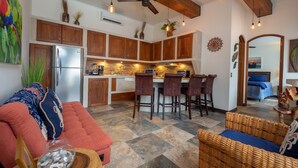 A modern kitchen with wooden cabinets, a stainless steel refrigerator, and a bar area with wicker chairs. - Luxury Beachfront Mar Arena 2 (Jacó)