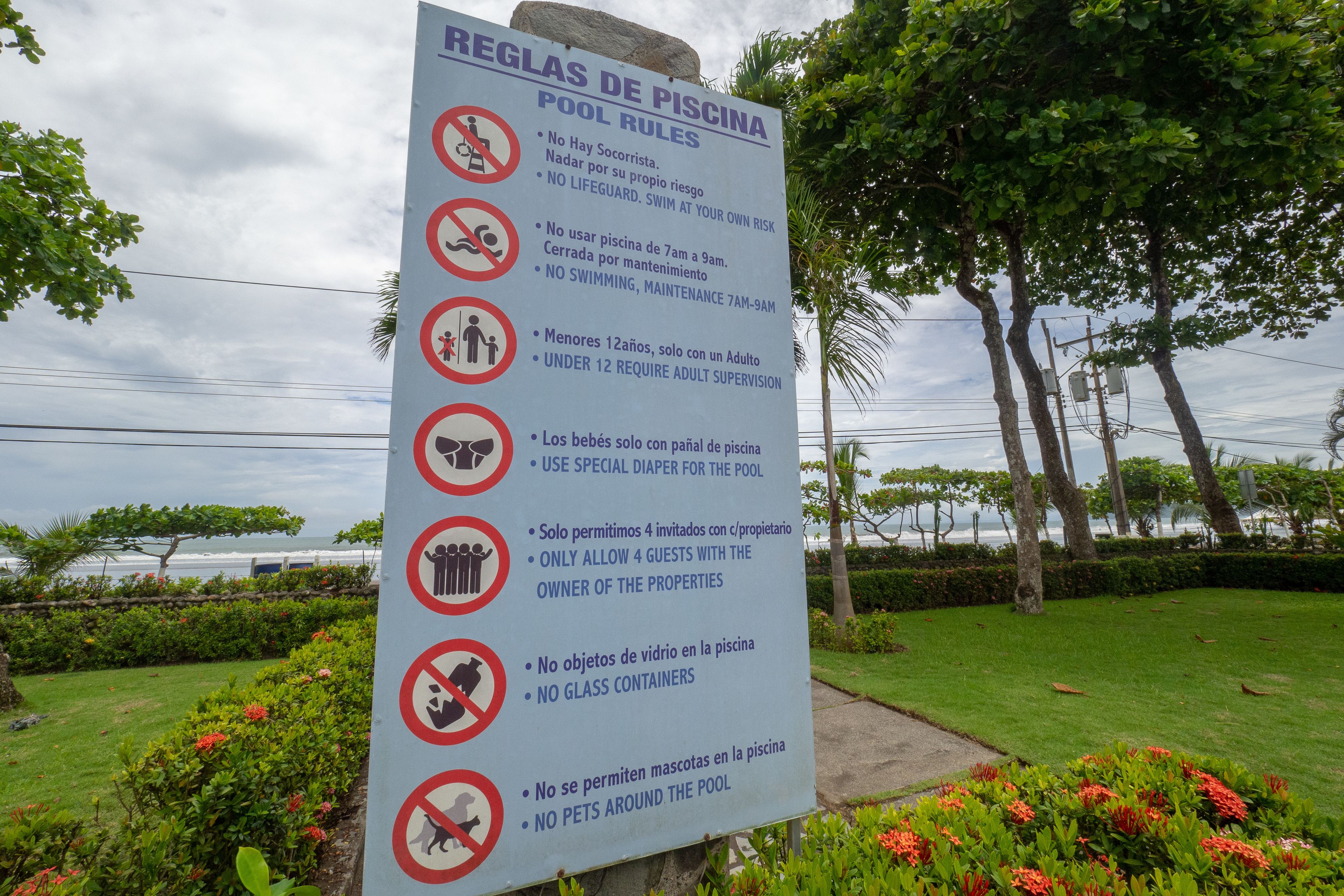 Letrero que enumera las normas de la piscina en español, incluyendo prohibido nadar, prohibido llevar recipientes de vidrio y no se admiten mascotas.