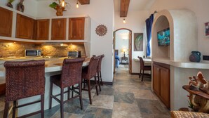 A kitchen with a stone backsplash, wooden cabinets, and a central island with bar stools. - Luxury Beachfront Mar Arena 2 (Jacó)