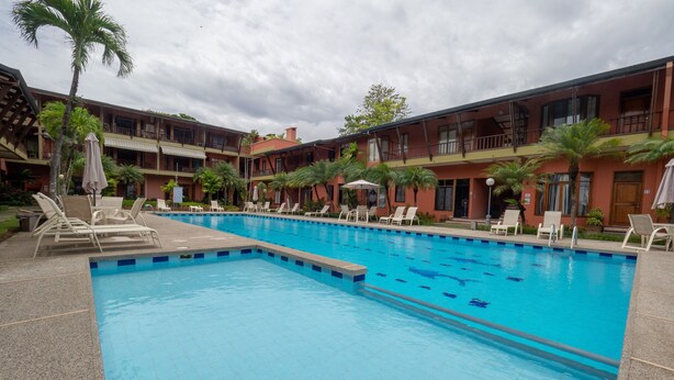 A swimming pool with lounge chairs and umbrellas, surrounded by a multi-story building with balconies. - Luxury Beachfront Mar Arena 2 (Jacó)