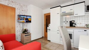 Ein kompakter Wohnbereich mit Küchenzeile, einem an der Wand befestigten Fernseher und einem roten Sofa.