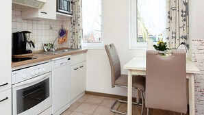Eine kleine Küche mit weißen Geräten, einer Holzarbeitsplatte und einem Essbereich mit Tisch und Stühlen.