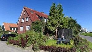 Ein zweigeschossiges Backsteinhhaus mit rotem Ziegeldach, umgeben von einem gepflegten Garten mit verschiedenen Sträuchern und einem Trampolin.