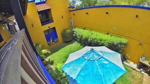 Un patio con un paraguas azul, paredes amarillas y plantas verdes.