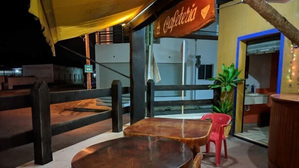 Un espacio al aire libre con mesas y sillas de madera, un letrero que dice "Cafetería" y una planta en maceta.