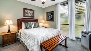 A bedroom with a bed, two bedside tables with lamps, a ceiling fan, a bench, and a window with blinds. - 🏖️Beautiful Ocean Views | Top Floor | Concierge Included (Kailua Kona)