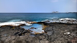 A rocky shoreline with a large cruise ship in the distance. - 🏖️Beautiful Ocean Views | Top Floor | Concierge Included (Kailua Kona)