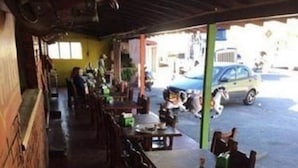 An outdoor cafe with wooden tables and chairs, a brick wall on one side, and a view of the street with parked cars.