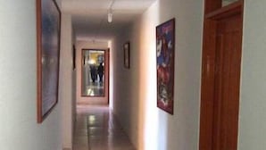 A corridor with tiled flooring, framed pictures on the walls, and a wooden door at the end.