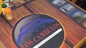 A wooden table with a circular logo for "Los Caminos Hotel Restaurante" and a filmstrip design around the logo.