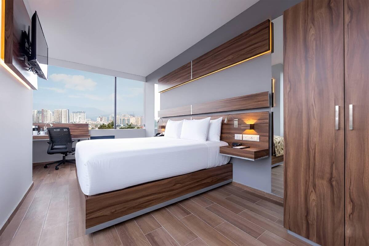 A modern bedroom with a large bed, a desk, and a city view.