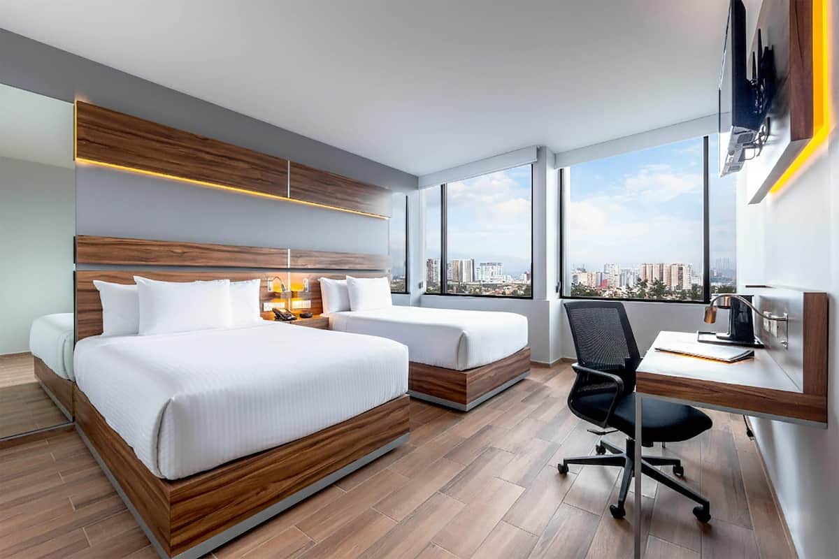 A hotel room with a large bed, a desk, and a view of the city.