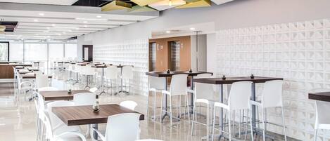 A modern dining area with white chairs and tables, geometric ceiling design, and a patterned wall.
