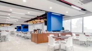 A modern, well-lit dining area with white chairs, a wooden table, and a central island with kitchen appliances.