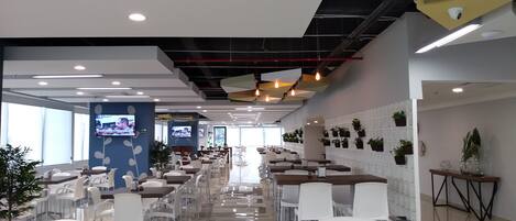 Um restaurante moderno com mesas e cadeiras compridas, várias TVs na parede e plantas em vasos nas paredes.