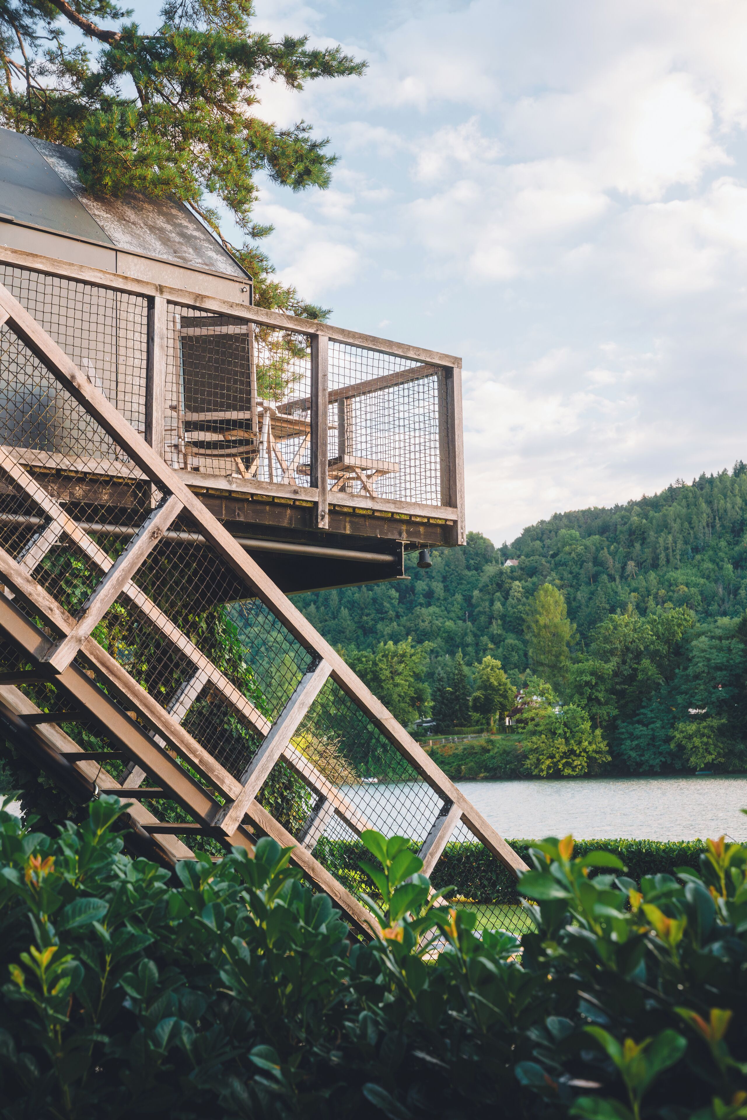 A wooden deck with a metal railing overlooking a lake, surrounded by greenery.