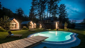 Une piscine privée avec une terrasse en bois, entourée d’une pelouse bien entretenue et d’arbres.