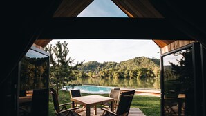 Une terrasse en bois avec une table et des chaises, donnant sur un lac et des collines boisées.