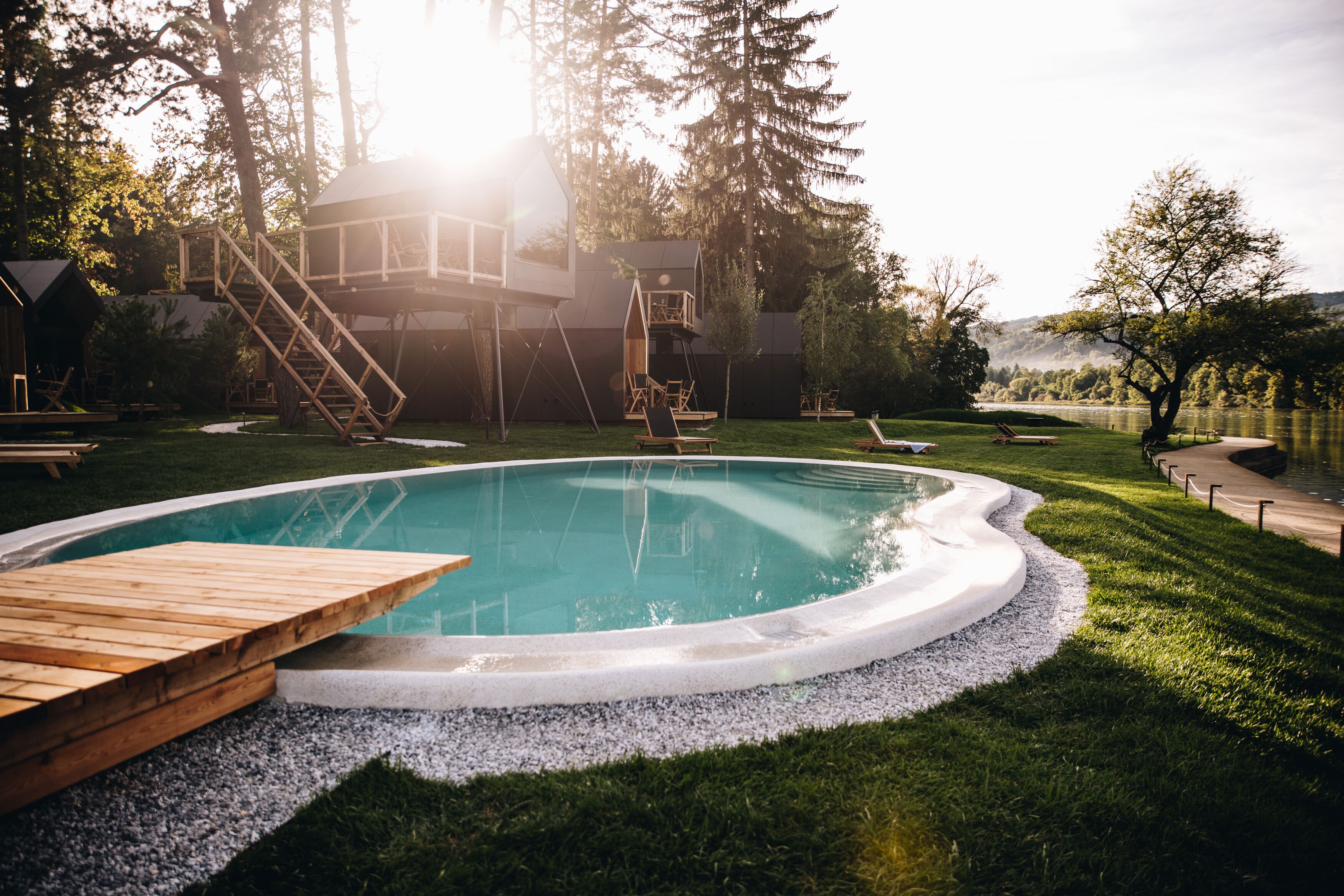 A swimming pool with wooden deck seating, surrounded by a grassy area and trees.