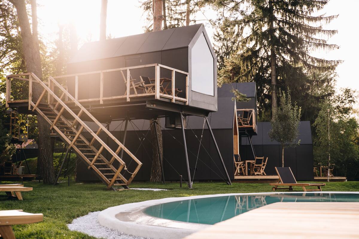 Un espace piscine extérieur moderne, doté d’une terrasse en bois, d’une petite structure en bois surélevée avec un balcon et offrant une vue dégagée sur les arbres environnants.