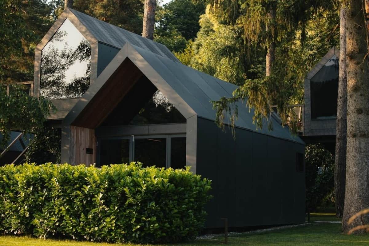 Une maison moderne avec un toit en pente, de grandes fenêtres et entourée de verdure.
