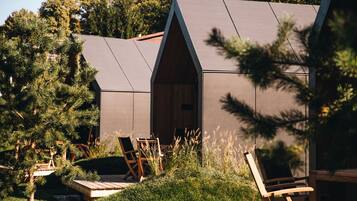 A modern cabin with a sloped roof, surrounded by a well-maintained garden and outdoor seating area.