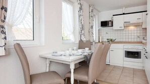A kitchen with white cabinets, a microwave, and a stove. There is a dining table with chairs and a window with curtains.